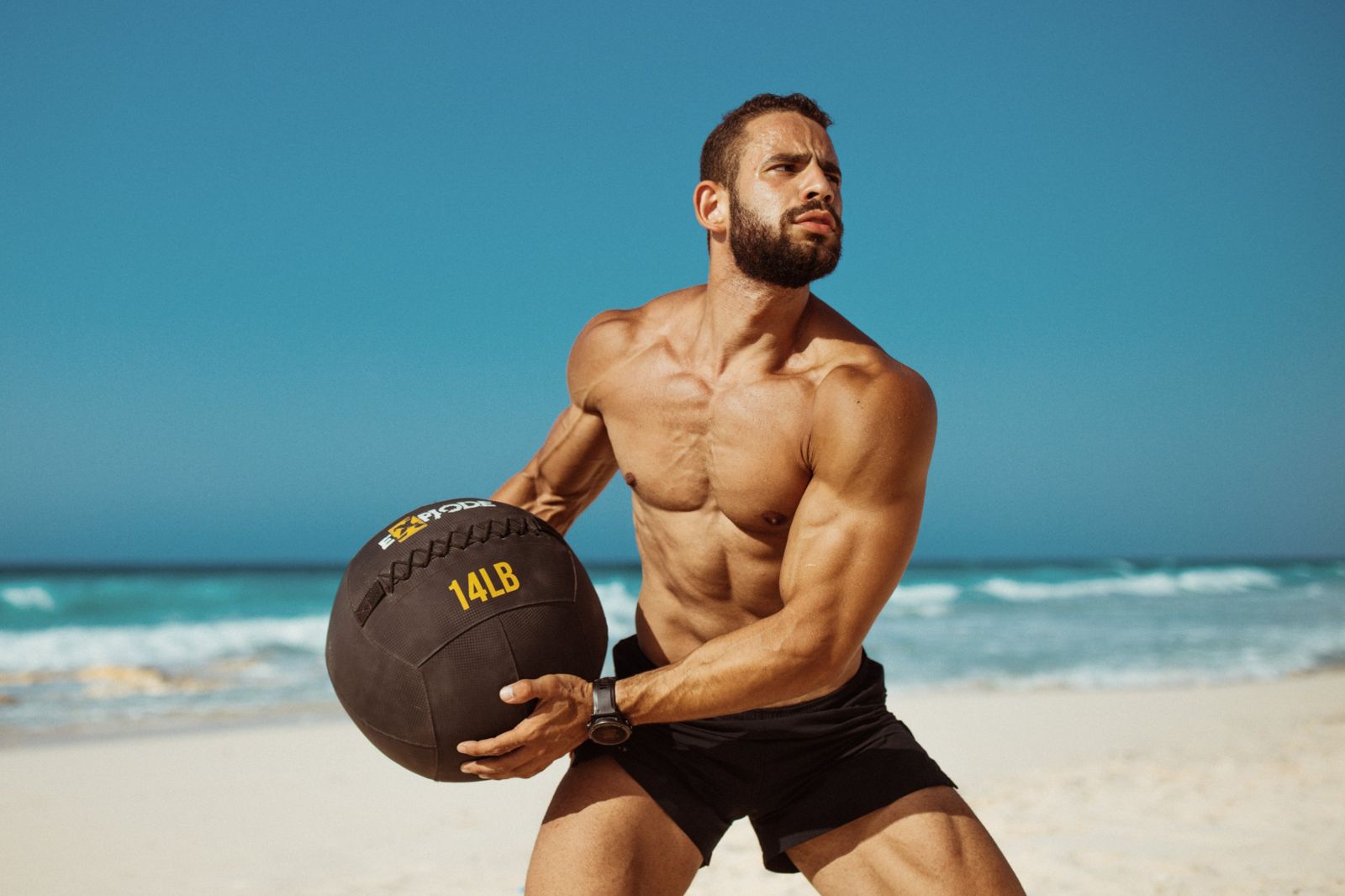 An athlete swinging a medicine ball on the beach